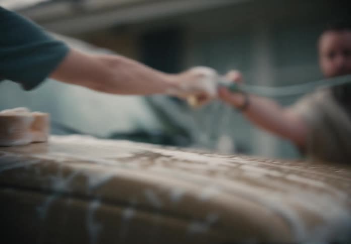 A young man washes a golden pickup truck in slow motion, scrubbing with a sponge and then rinsing with a hose