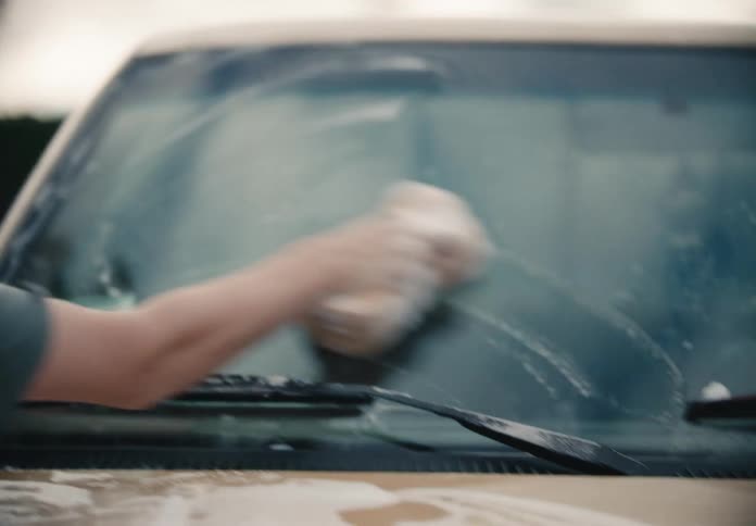 Teenage boy carefully washes the windshield of a car with a soapy sponge in slow motion