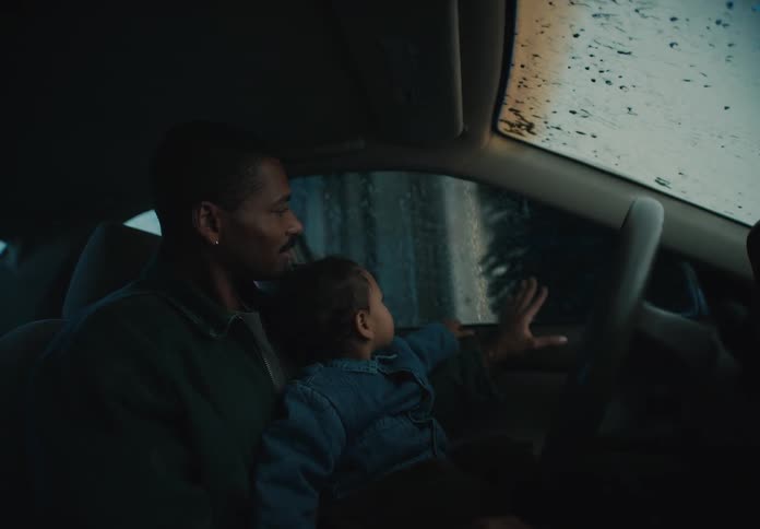 A smiling father shows his curious toddler the sights and sounds of an automatic car wash from inside their vehicle