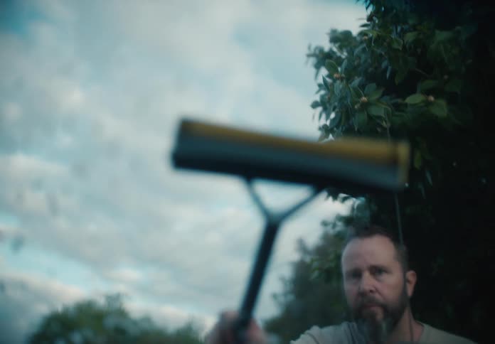A bearded man washes a car windshield with a squeegee in slow motion as seen from inside the car