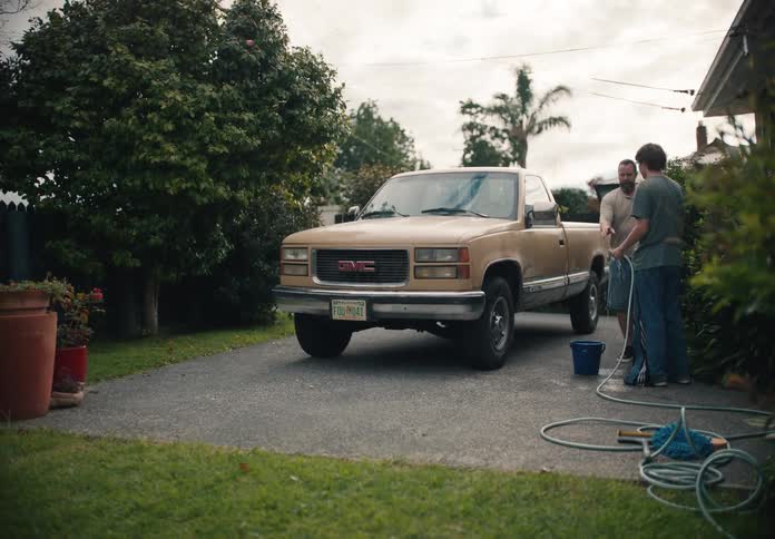 A father and son wash a tan pickup truck together in the driveway of their suburban home