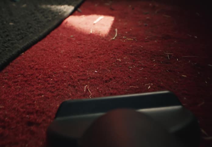POV shot in slow motion of a vacuum cleaner sucking up dirt and debris from a red car carpet