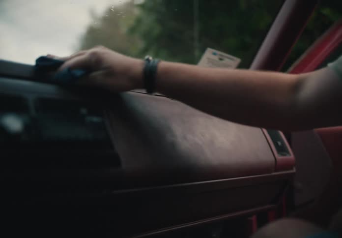 A man's hand carefully wipes dust off the dashboard of a vintage red car with a blue cloth