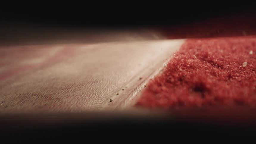 A vacuum cleaner nozzle sucks up dirt and debris from a red carpet in a car interior macro shot