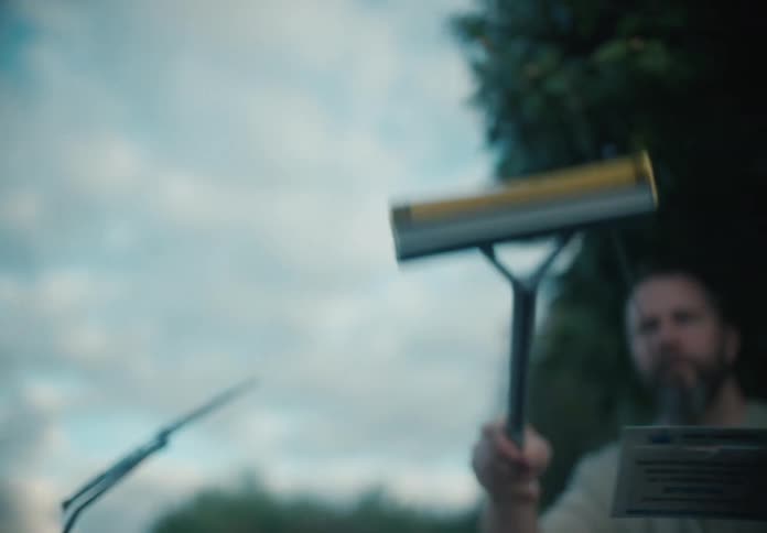 Cinematic slow-motion interior shot of a man cleaning a car's windshield with a squeegee against a cloudy sky