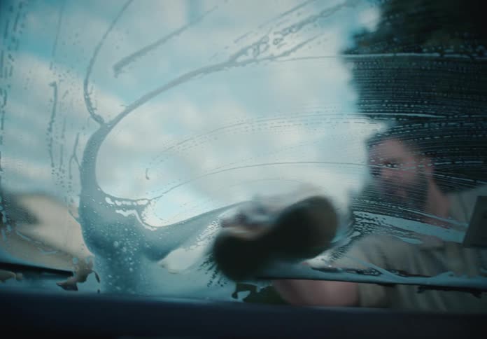 Interior shot from inside a car looking out as a man washes the soapy windshield with a sponge