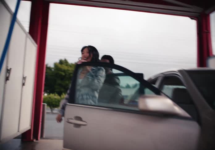 A happy young woman with glitter on her face gets out of a car with her friend at a car wash