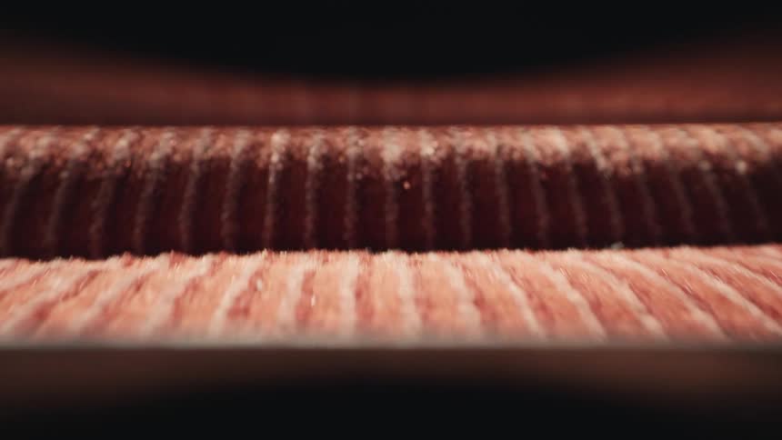 A macro shot shows a reddish, granular substance moving along a vibrating conveyor belt in a processing facility
