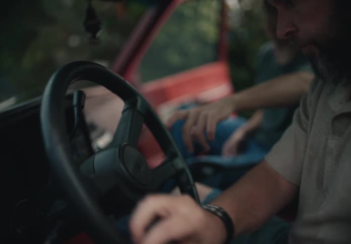 A man carefully cleans the steering wheel of his vintage red truck with a cloth