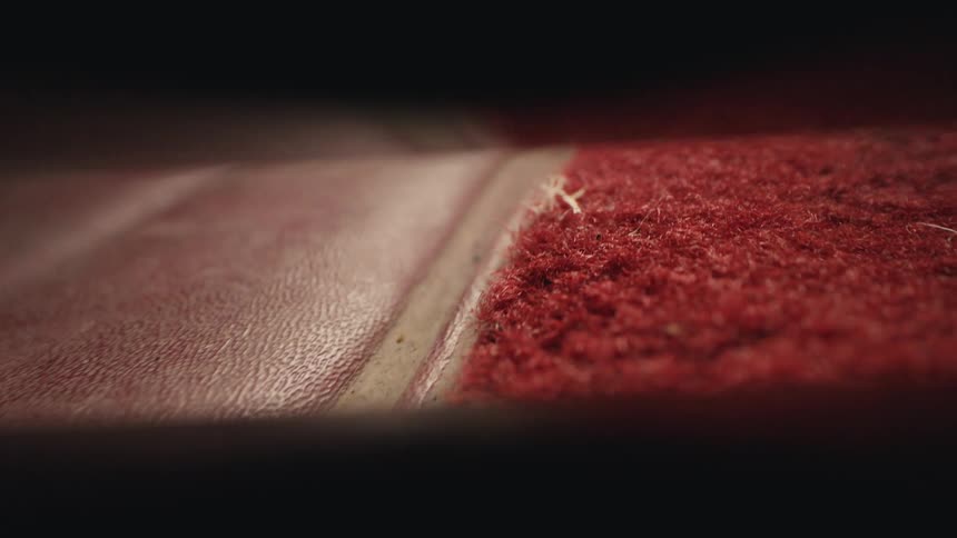 A revealing macro shot travels along the dusty, worn seam between red carpet and leather upholstery