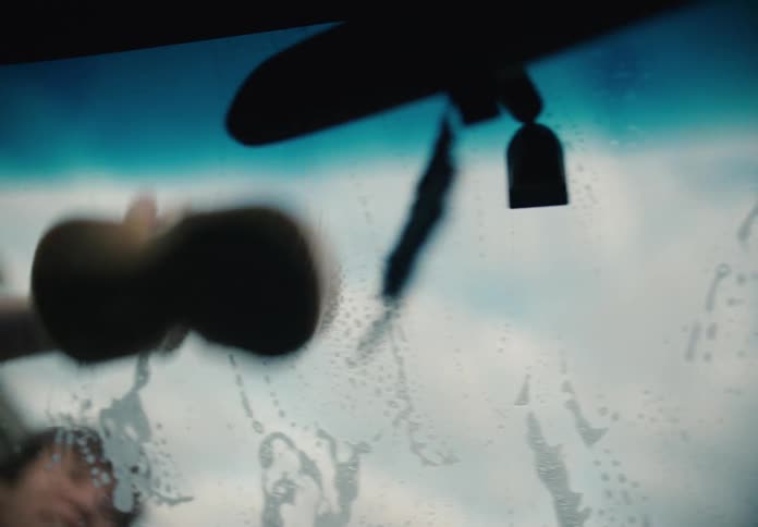 Artistic slow-motion shot from inside a car as a person washes the sudsy windshield with a sponge