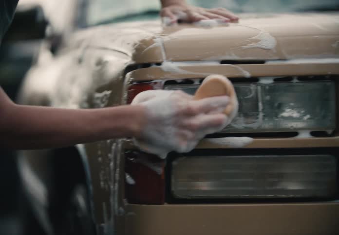 A teenage boy diligently washes his vintage pickup truck in the driveway in slow motion