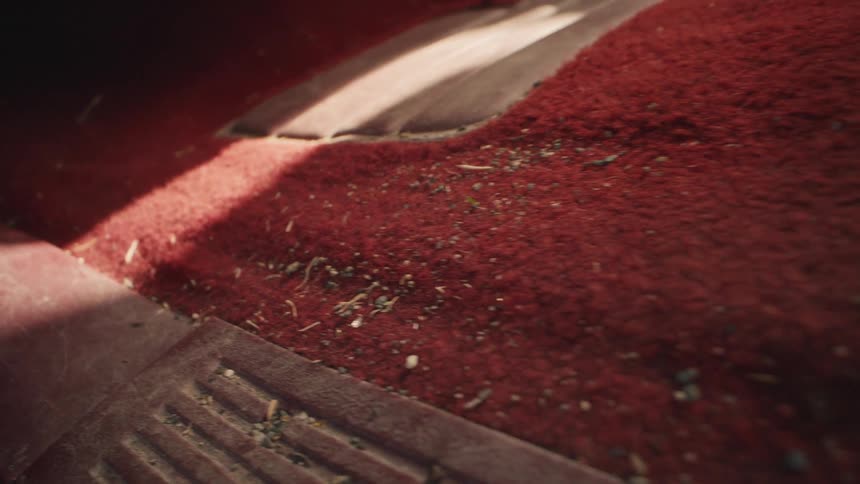 Extreme close-up shot slowly pulling back from a dirty, red, carpeted car floor full of crumbs and debris