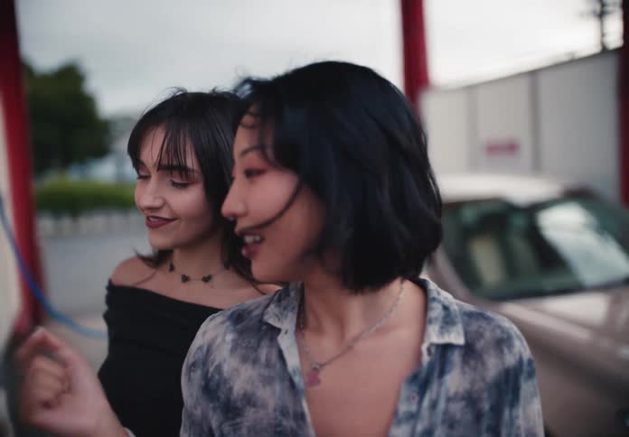A close-up of two happy young women smiling and talking while at an outdoor car wash