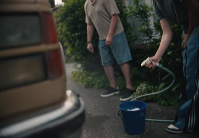 A father and teenage son wash a car together in the driveway in a cinematic slow-motion shot