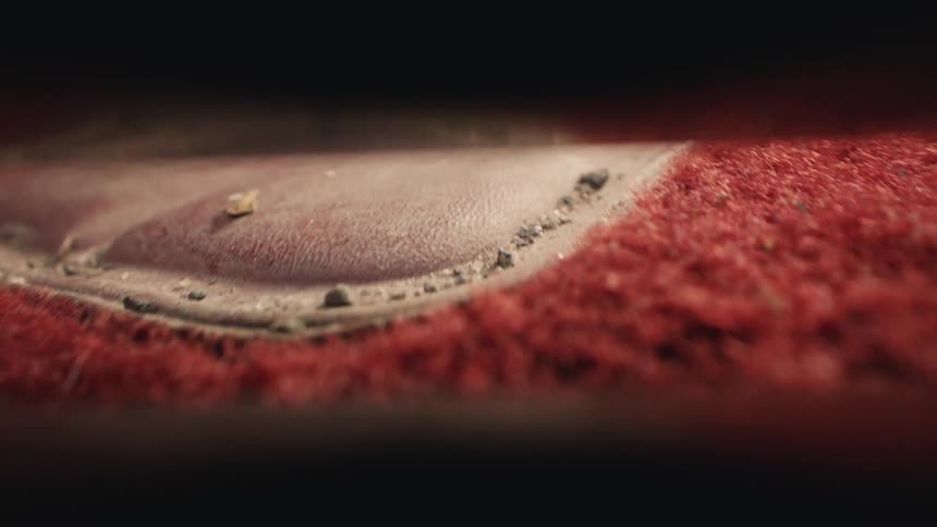 Satisfying macro view of a vacuum nozzle sucking up dirt and debris from a red car floor mat