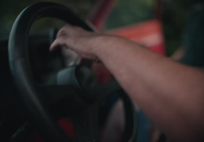 A close-up shot of a person using a cloth to wipe down and clean the steering wheel of a classic red truck