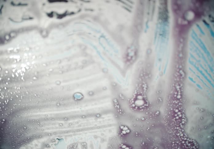 Abstract point-of-view from inside a car of colorful pink and white soap suds sliding down the windshield at an automatic car wash