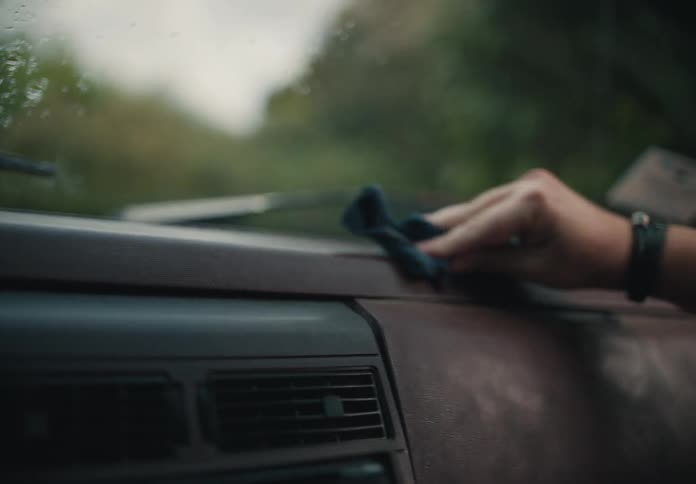 A close-up shot shows a hand carefully cleaning the dashboard of a vehicle with a cloth in slow motion