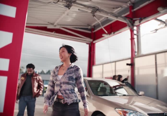A stylish young woman and her friends get out of their car and prepare to wash it at a self-service station in slow motion