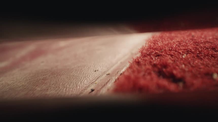 Slow-motion macro view of a vacuum cleaner powerfully sucking dirt, dust, and debris from a dirty red carpet