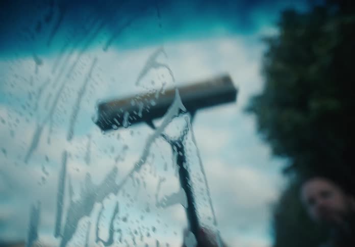 Close-up slow motion shot of a squeegee wiping soap suds from a car windshield