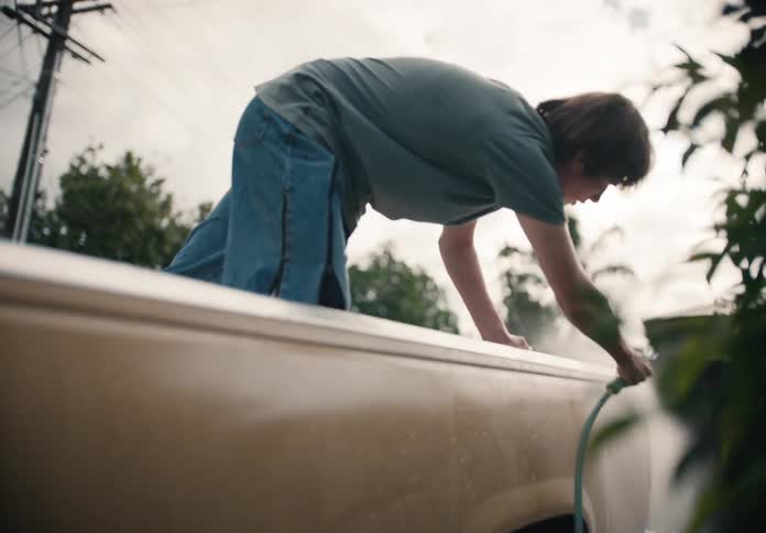 Slow motion footage of a young man in the back of a truck washing the vehicle with a water hose