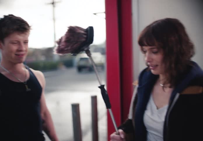 A stylish young woman grabs a brush at a car wash and smiles as her friends join her in slow motion
