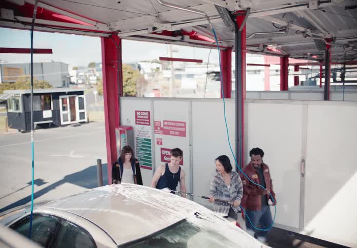 A diverse group of young friends have fun washing their car together at a self-service car wash bay
