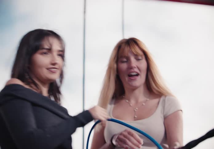 Two joyful friends laugh and point while washing a car together at a self-service station in slow motion