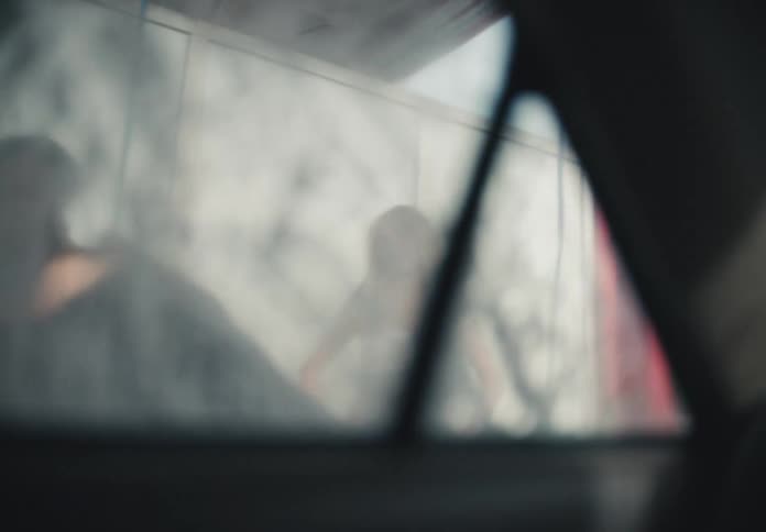 A group of diverse friends joyfully wash a car, seen through the soapy windshield from the inside