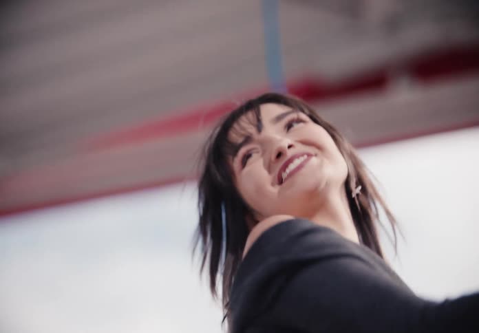 A slow-motion, low-angle shot of a beautiful young woman with dark hair laughing with genuine joy
