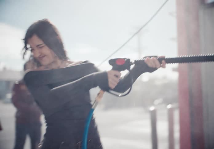 Edgy young woman spraying a power washer at a car wash in slow motion on a sunny day
