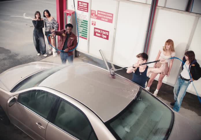 From a high angle, a group of young, stylish friends have fun washing a car together in slow motion at a coin-operated car wash