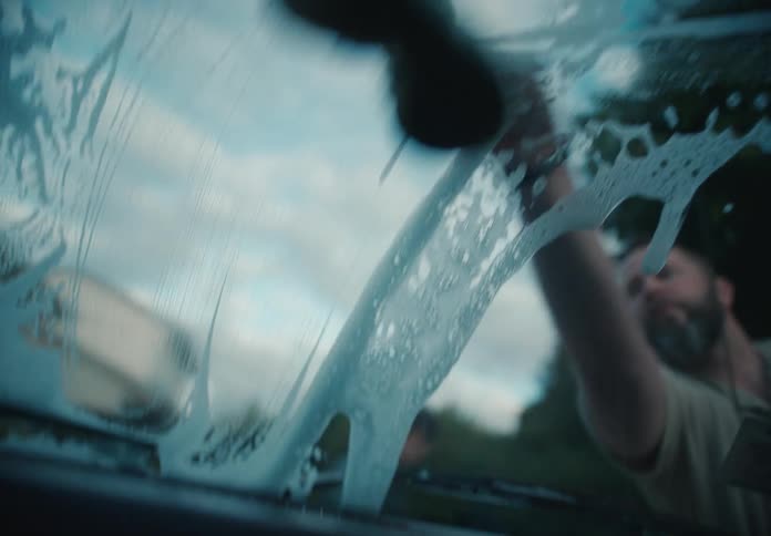View from inside a car as a man washes the soapy windshield with a sponge in slow motion