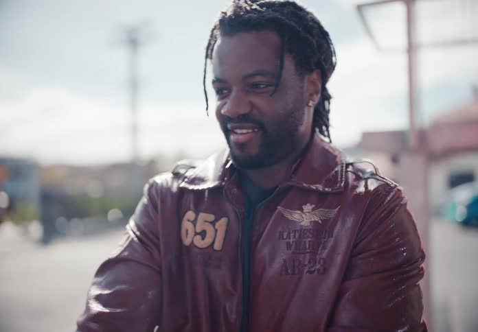 A stylish man in a leather jacket smiles happily before his expression changes to playful surprise