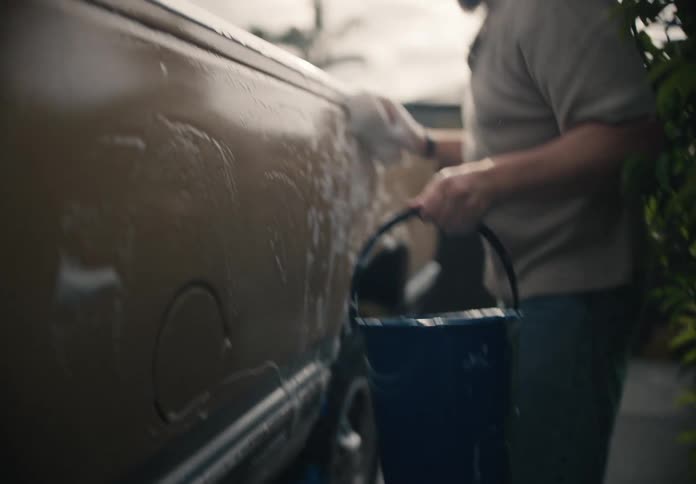 Slow motion shot of a man holding a bucket and sponge while carefully washing the side of his pickup truck