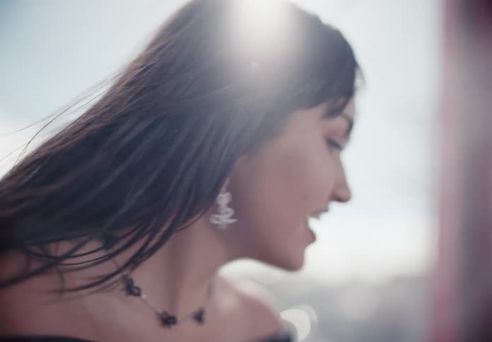 Close-up slow motion shot of a joyful young woman with braces smiling as the wind blows her hair in the bright sunlight