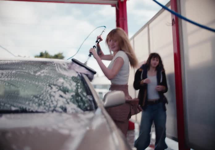 Young women have fun together washing a car at a self-service car wash in slow motion