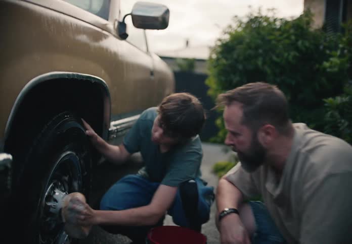 A low-angle push-in shot reveals a father and his son bonding as they wash a truck together in the driveway