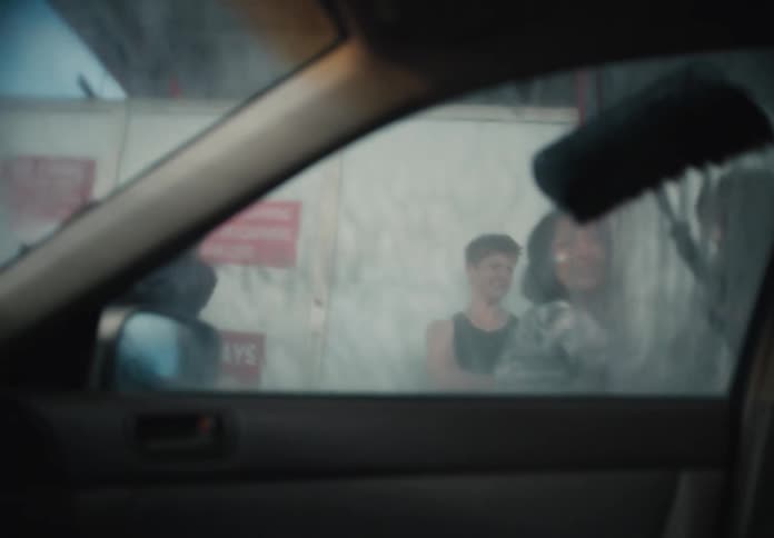 Point of view from inside a car as a group of friends playfully clean the soapy window at a self-service car wash
