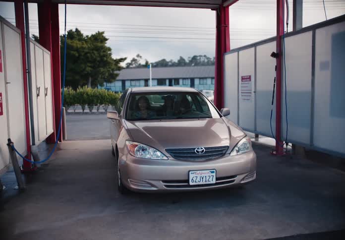A gold sedan pulls into a self-service car wash bay, and a diverse group of smiling young friends gets out