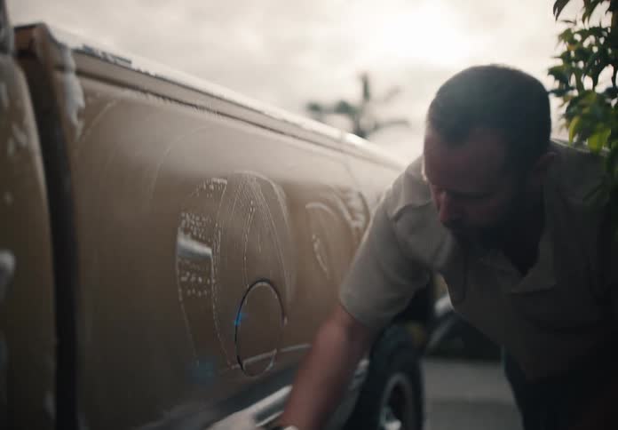 A man carefully washes the side of his truck with a soapy sponge in his driveway