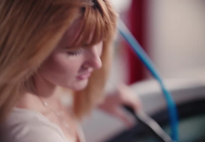 A woman with flowing blonde hair charges her electric car at a modern charging station in slow motion