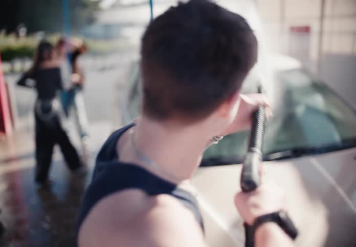 Dreamy slow motion shot from behind of a young man washing his car with a pressure washer
