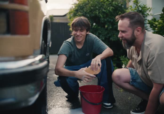 A father and his teenage son have a conversation while washing a car together in the driveway