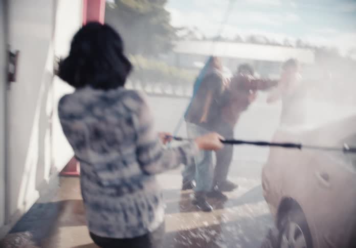 A group of happy friends playfully wash a car and spray each other with water in slow motion