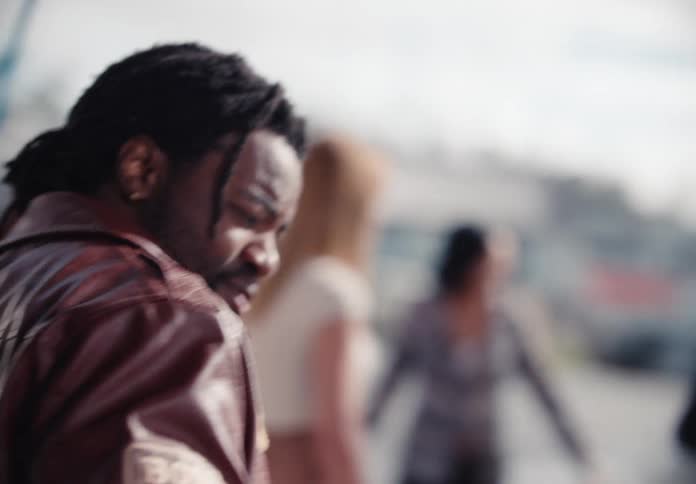 A stylish Black man with dreadlocks smiles while washing a car with pink soap in slow motion at an outdoor car wash