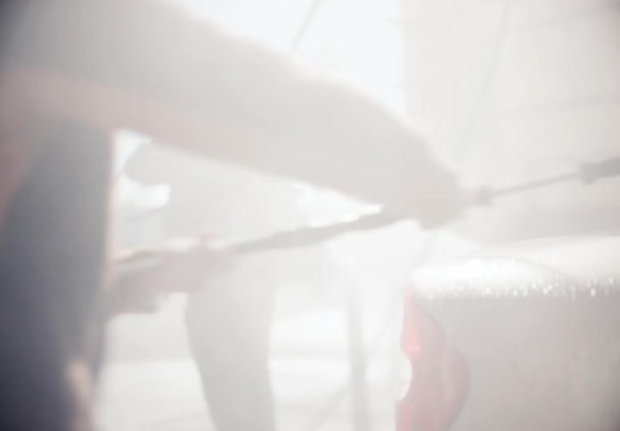 Slow motion shot of a smiling couple playfully washing their car at a sunny, outdoor car wash