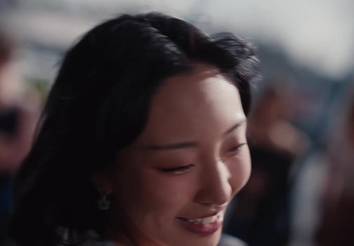 A slow-motion close-up captures a young Asian woman's joyful expression as she uses a rowing machine during an outdoor workout class